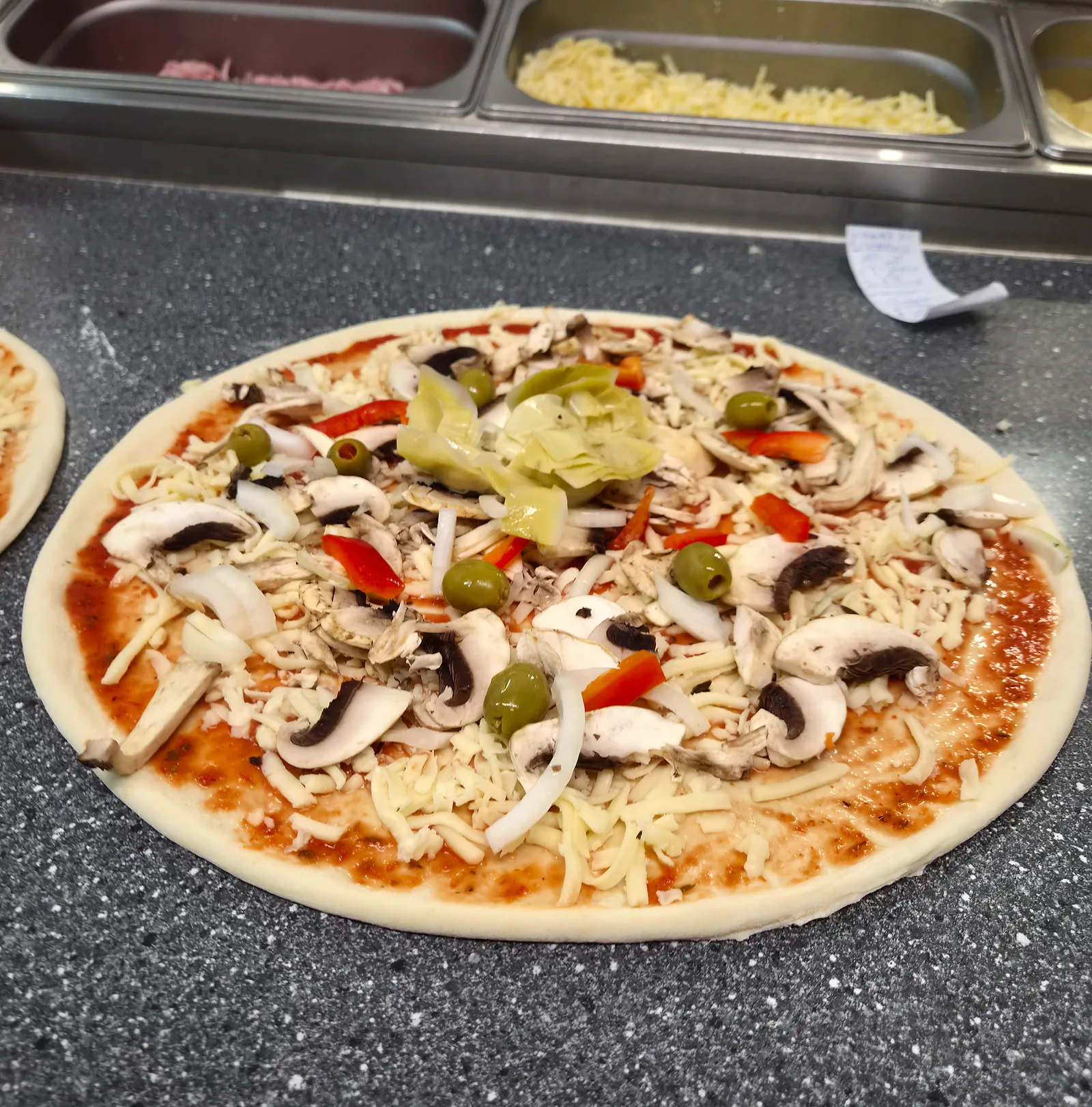 Pizza med champinjoner, paprika, oliver och kronärtskocka innan den går in i ugnen